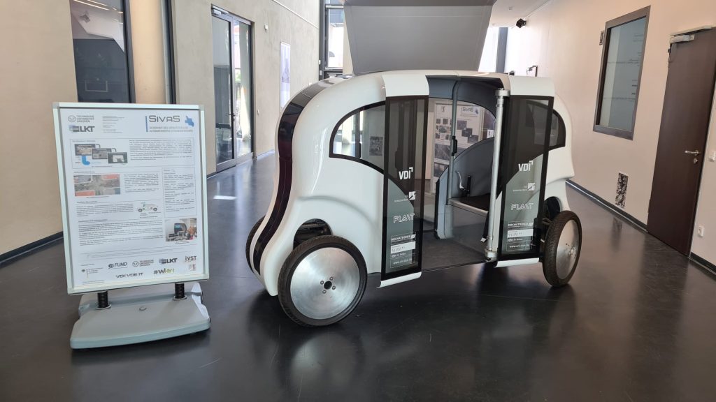 Im Foyer des Bürgerzentrums steht der Prototyp eines automatisierten Kleinbusses und daneben eine Infotafel.