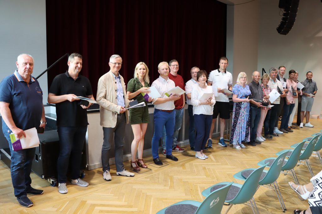 17 Mitglieder des Stadtrates Hoyerswerda stehen vor einer Bühne und lächeln in die Kamera.